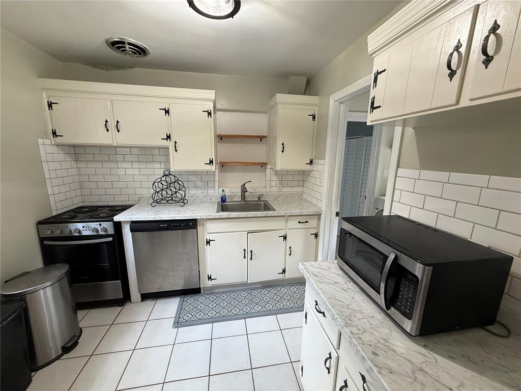 A kitchen with white cabinets, subway tile backsplash, marble-look countertops, and stainless steel appliances — 313 NW 34TH DRIVE, GAINESVILLE, FL