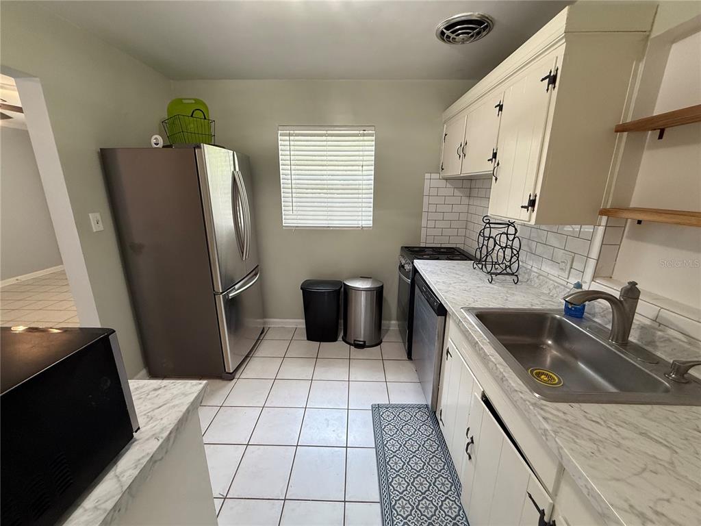 A kitchen features white cabinets, a stainless steel refrigerator, a sink, and tiled flooring — 313 NW 34TH DRIVE, GAINESVILLE, FL