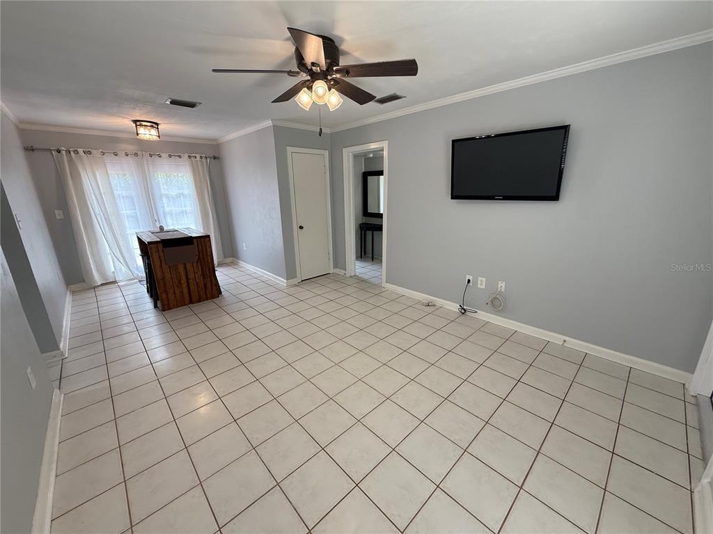 A room with light gray walls, white tile flooring, a ceiling fan, and a wall-mounted television — 313 NW 34TH DRIVE, GAINESVILLE, FL