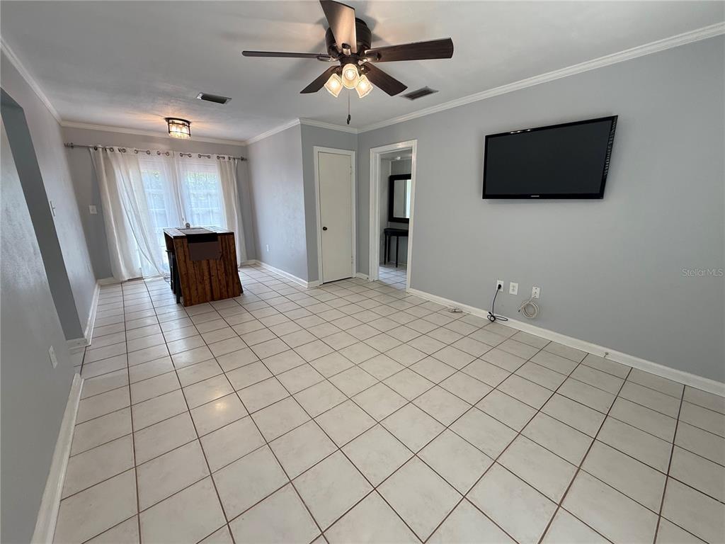 A living room with light gray walls, white tile flooring, a ceiling fan, and a wall-mounted television — 313 NW 34TH DRIVE, GAINESVILLE, FL
