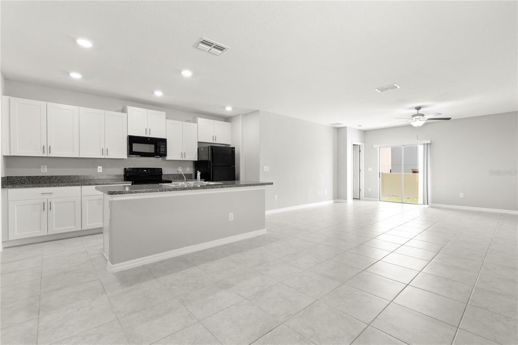 An open-concept kitchen with white cabinets and a granite island overlooks a tiled living area — 10217 SUMMER KISS AVENUE, RIVERVIEW, FL