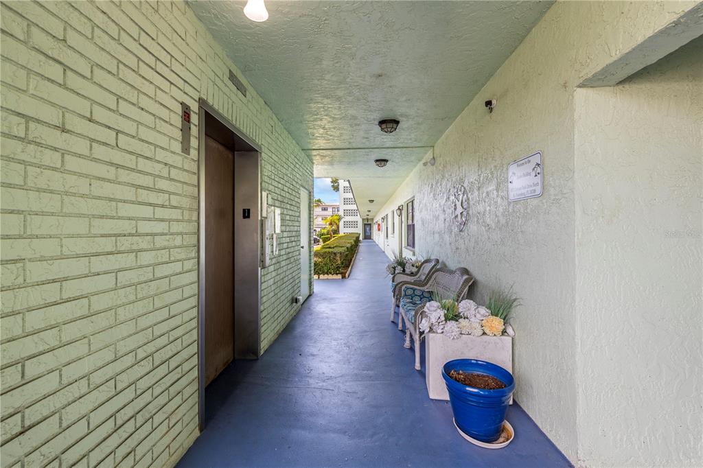 An outdoor hallway features a brick wall, an elevator, and a seating area with chairs — 5973 TERRACE PARK DRIVE N UNIT 101, ST PETERSBURG, FL