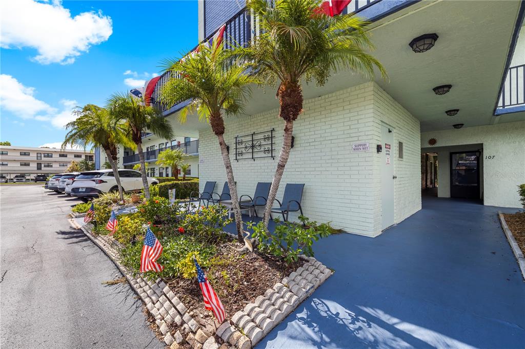 A low-rise apartment building exterior features a landscaped garden with small American flags and chairs — 5973 TERRACE PARK DRIVE N UNIT 101, ST PETERSBURG, FL