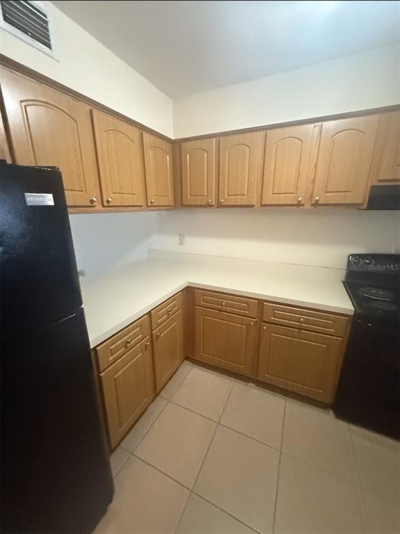 A kitchen features light wood cabinets, white countertops, black appliances, and light-colored floor tiles — 4113 S SEMORAN BOULEVARD UNIT 11, ORLANDO, FL