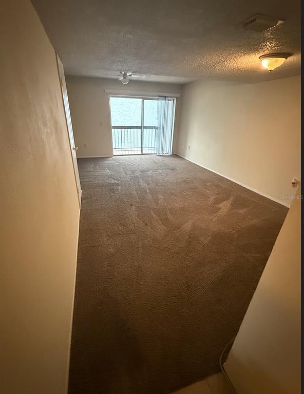 An empty living room features brown carpeting, beige walls, and a sliding glass balcony door — 4113 S SEMORAN BOULEVARD UNIT 11, ORLANDO, FL