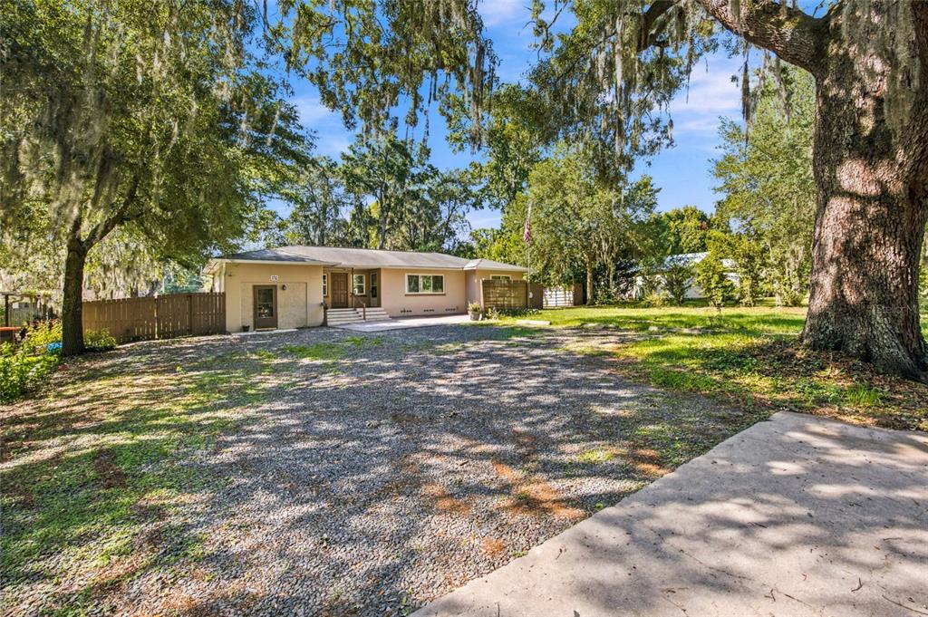 A single-story house with a gravel driveway and large oak trees in the front yard — 5762 S AGNEW ROAD, BELLEVIEW, FL