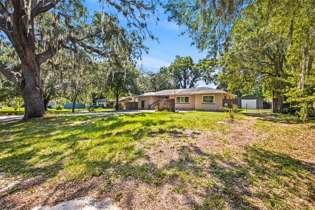 A single-story house with a tan exterior sits on a large, tree-shaded grassy lot — 5762 S AGNEW ROAD, BELLEVIEW, FL