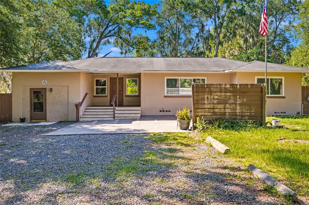 A single-story house with a gravel driveway, a wooden privacy screen, and an American flag — 5762 S AGNEW ROAD, BELLEVIEW, FL