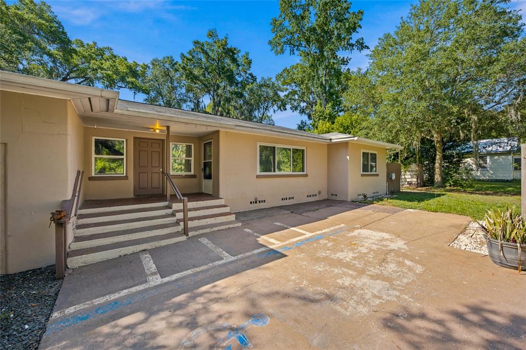 The exterior of a tan, single-story building features a concrete parking area and front steps — 5762 S AGNEW ROAD, BELLEVIEW, FL