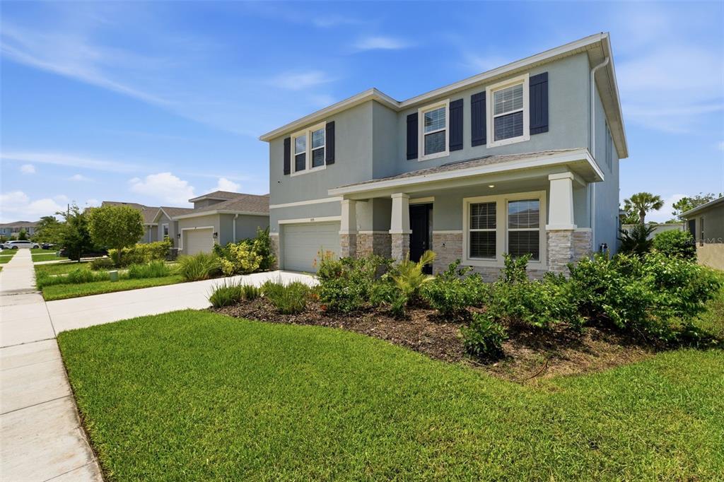 A two-story suburban house with a light blue exterior, stone accents, and a front lawn — 5715 WOODLAND SAGE DRIVE, SARASOTA, FL