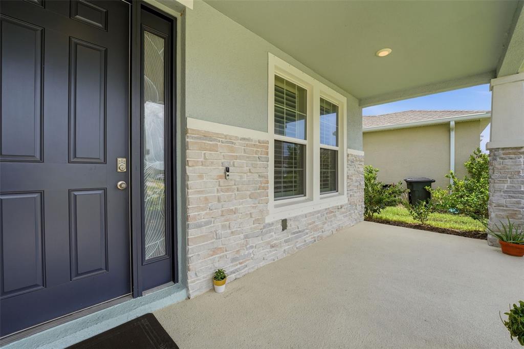 A covered front porch features a dark gray door, stone veneer siding, and two windows — 5715 WOODLAND SAGE DRIVE, SARASOTA, FL
