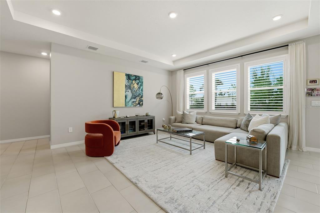 A living room features a large sectional sofa, an orange armchair, and a glass coffee table — 5715 WOODLAND SAGE DRIVE, SARASOTA, FL