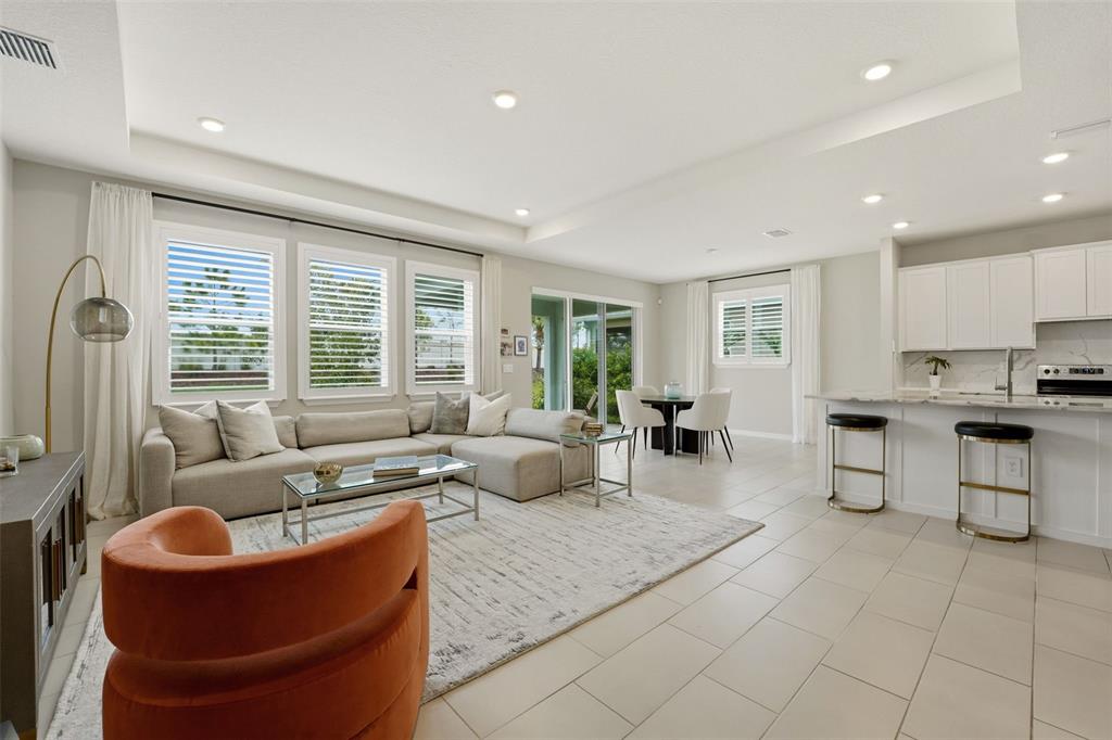 An open-concept living room features a sectional sofa, orange armchair, and an adjacent kitchen — 5715 WOODLAND SAGE DRIVE, SARASOTA, FL