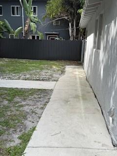 A concrete walkway runs alongside a white building wall toward a dark metal fence — 7640 NE 3rd Pl, Miami FL 33138, MIAMI, FL
