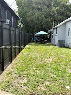 A narrow grassy backyard is bordered by a tall dark fence and a white house — 7640 NE 3rd Pl, Miami FL 33138, MIAMI, FL