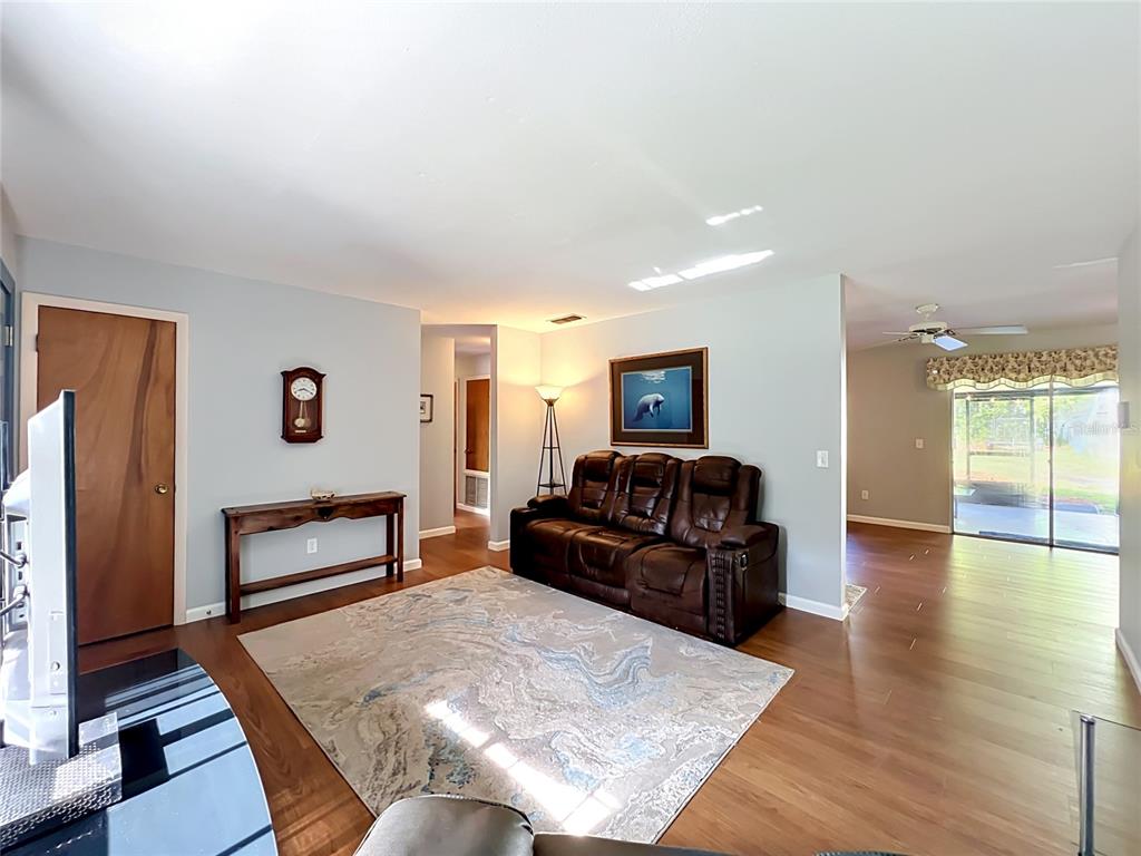 A living room features a brown leather sofa, wood flooring, and a wall-mounted clock — 7514 RIVERSIDE PLACE, ORLANDO, FL