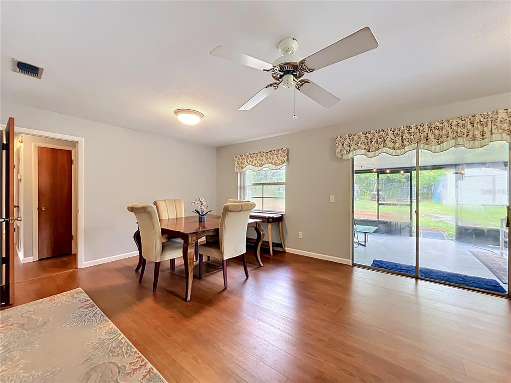 A dining room features wood-look flooring, a ceiling fan, and sliding glass doors to a patio — 7514 RIVERSIDE PLACE, ORLANDO, FL