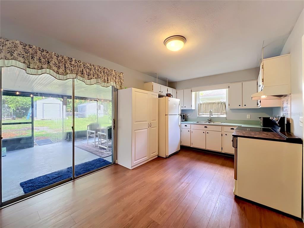 A kitchen with white cabinets, wood-look flooring, and a sliding glass door to a patio — 7514 RIVERSIDE PLACE, ORLANDO, FL