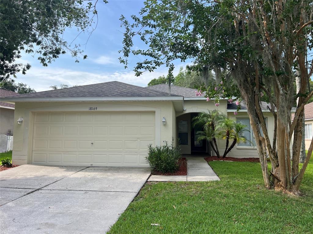 A single-story house with a two-car garage, light-colored stucco exterior, and a front walkway — 18169 SANDY POINTE DRIVE, TAMPA, FL