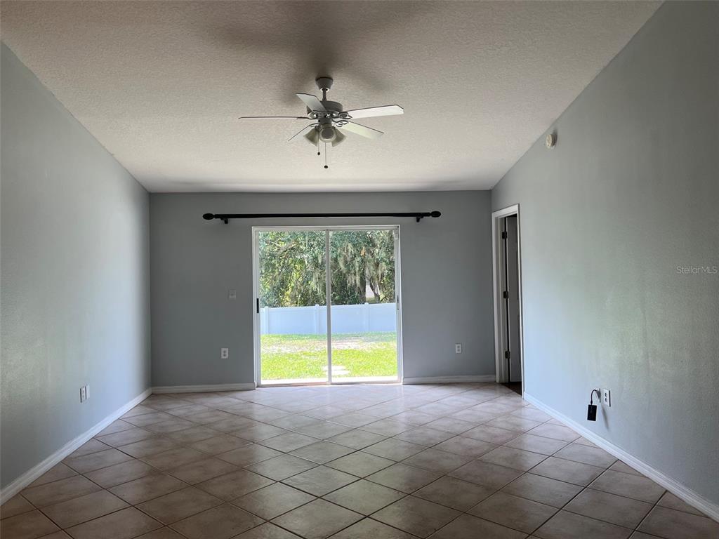 An empty room with light gray walls, tile flooring, a ceiling fan, and sliding glass doors — 18169 SANDY POINTE DRIVE, TAMPA, FL