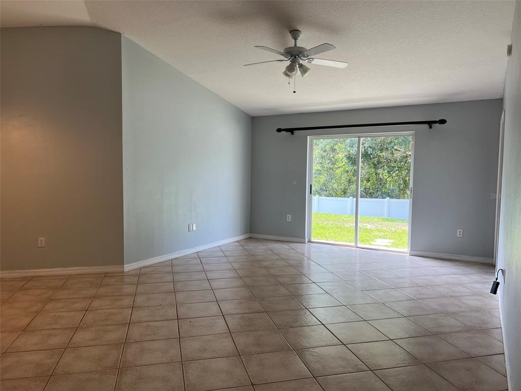 A living room with light blue walls, tile flooring, a ceiling fan, and sliding glass doors — 18169 SANDY POINTE DRIVE, TAMPA, FL