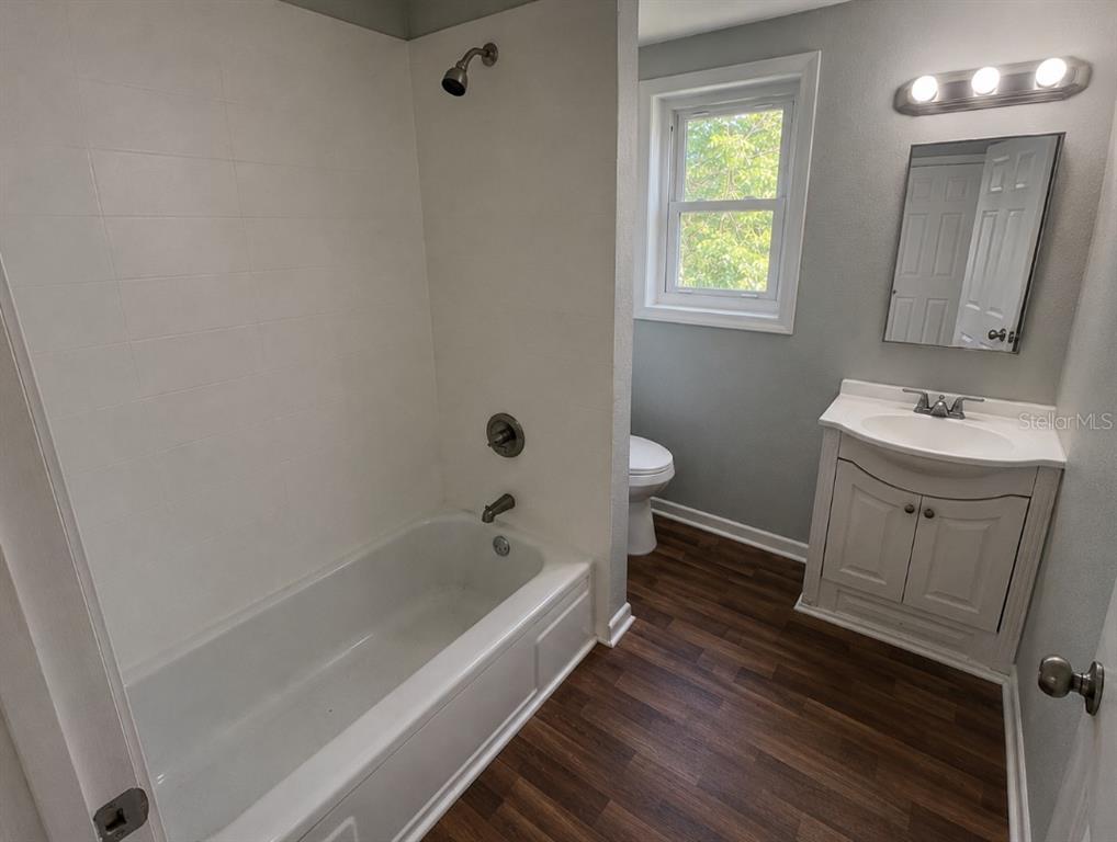 A bathroom features a white bathtub, a vanity with a sink, and wood-look flooring — 837 LAFAYETTE LANE, LAKELAND, FL