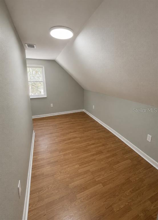 An attic room with light gray walls, wood-look flooring, a window, and a sloped ceiling — 837 LAFAYETTE LANE, LAKELAND, FL