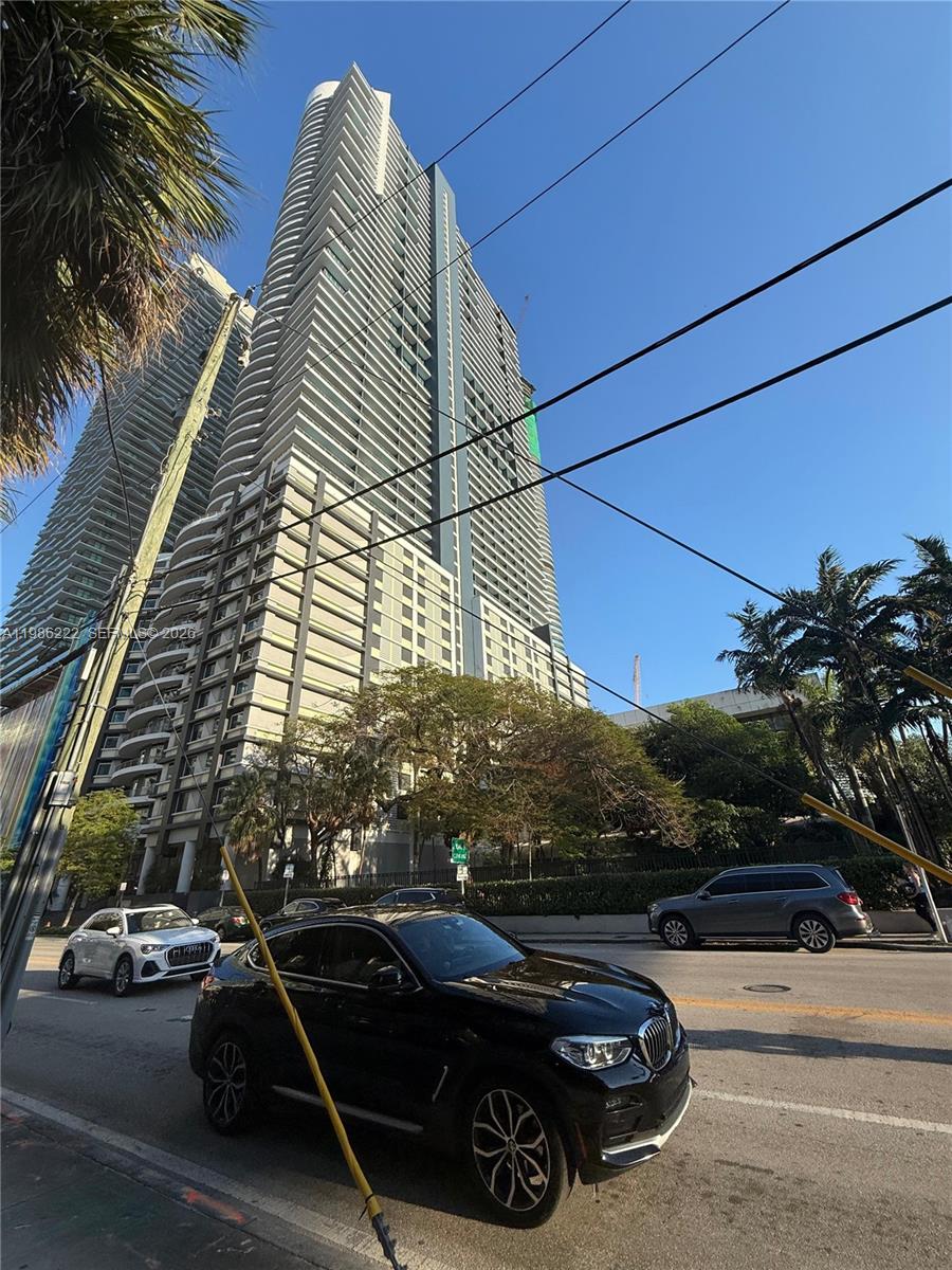 A low-angle exterior view of a tall modern residential skyscraper with a street and cars — 60 SW 13th St # 3017, Miami FL 33130, MIAMI, FL