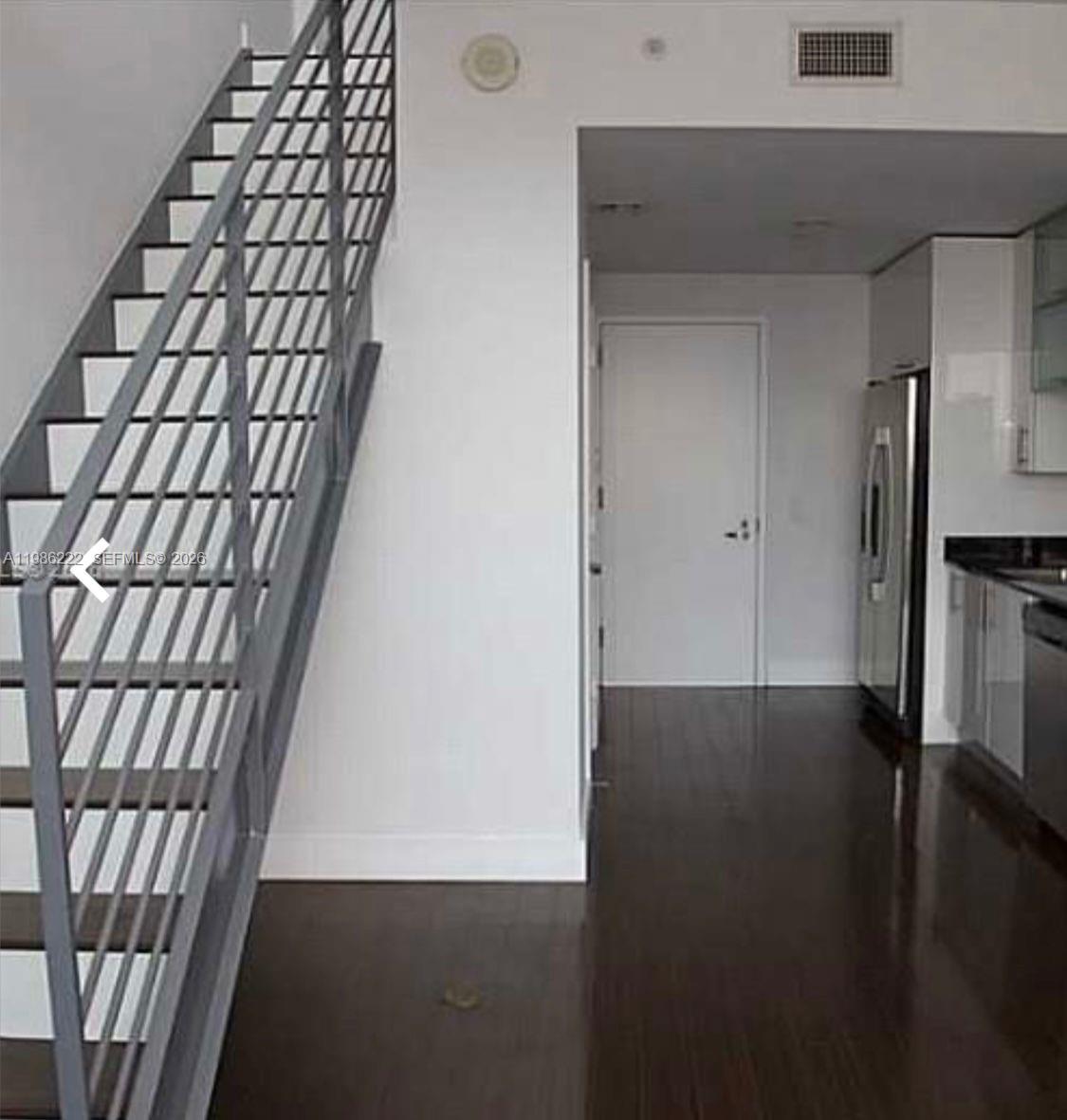 A modern interior features a metal staircase alongside a kitchen with dark wood flooring — 60 SW 13th St # 3017, Miami FL 33130, MIAMI, FL