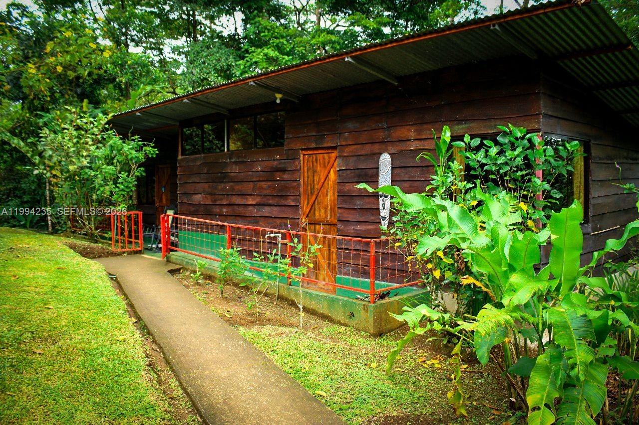 A rustic wooden cabin with a metal roof sits beside a concrete walkway and garden — Distrito 14 San Lorenzo, FL A-0190479, FL
