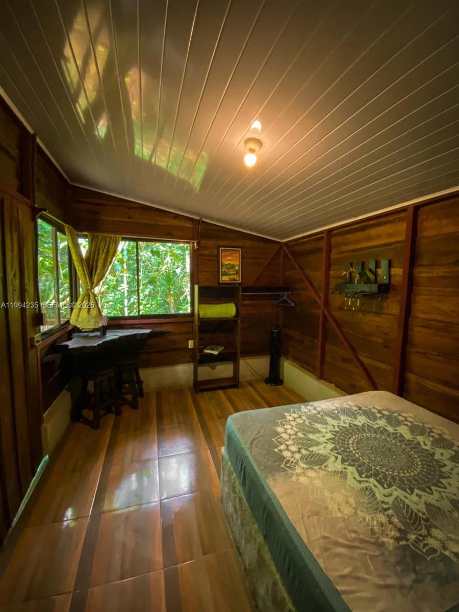 A bedroom with wood-paneled walls, a bed, and a window overlooking lush green trees — Distrito 14 San Lorenzo, FL A-0190479, FL