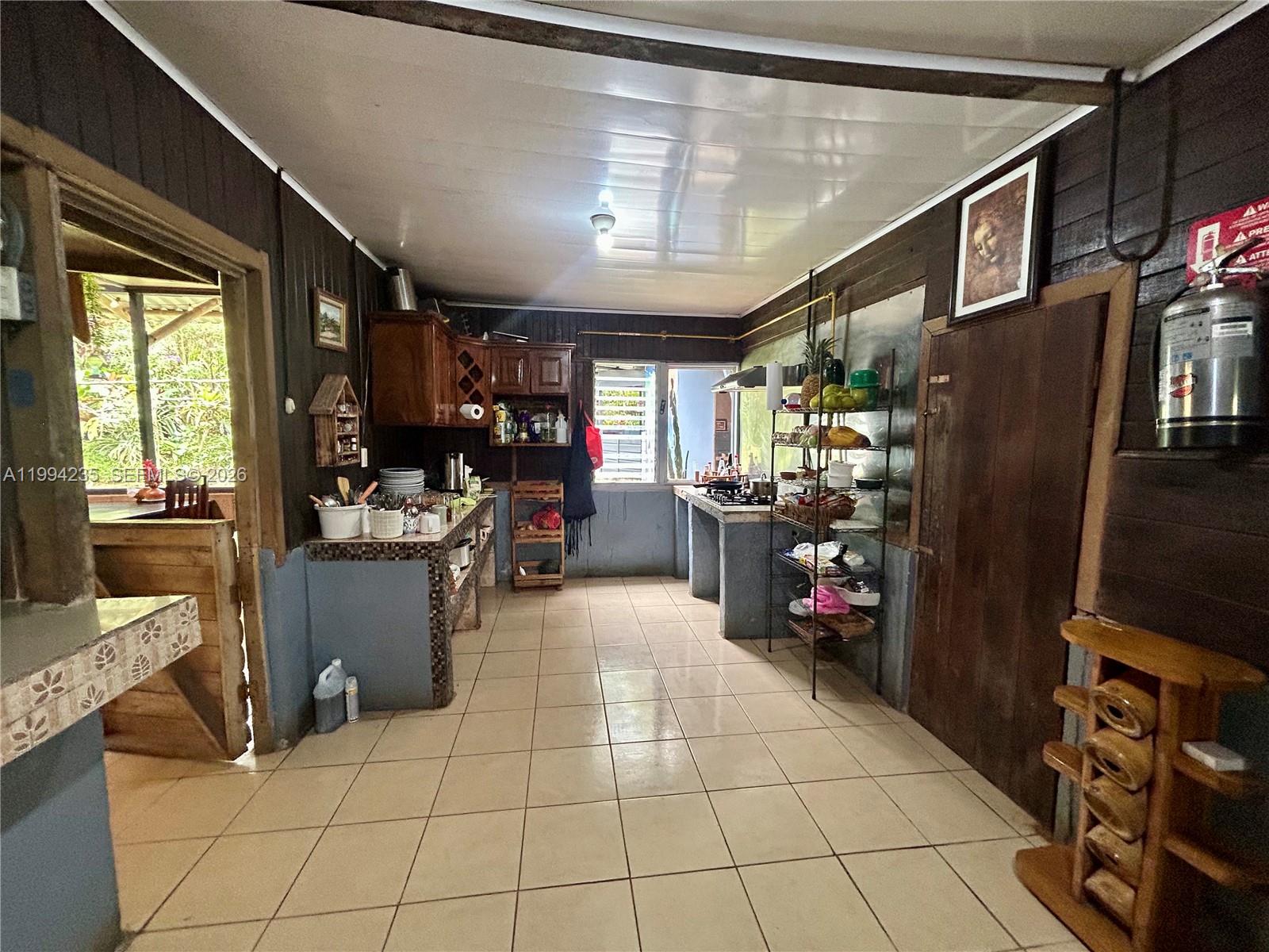 A rustic kitchen features dark wood walls, tiled floors, open shelving, and a tiled counter — Distrito 14 San Lorenzo, FL A-0190479, FL