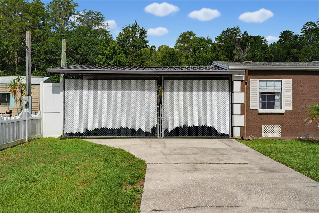 A concrete driveway leads to a carport enclosed by white privacy slats on chain-link fencing — 7421 HENRY DRIVE, LAND O LAKES, FL
