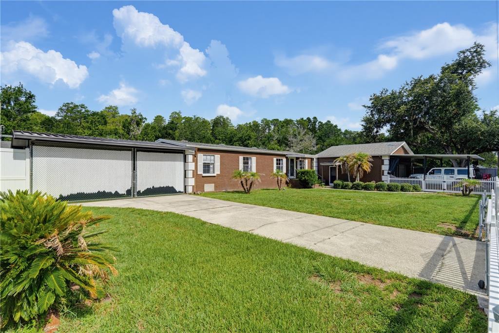 A single-story brick house with a white fence, a concrete driveway, and a carport — 7421 HENRY DRIVE, LAND O LAKES, FL