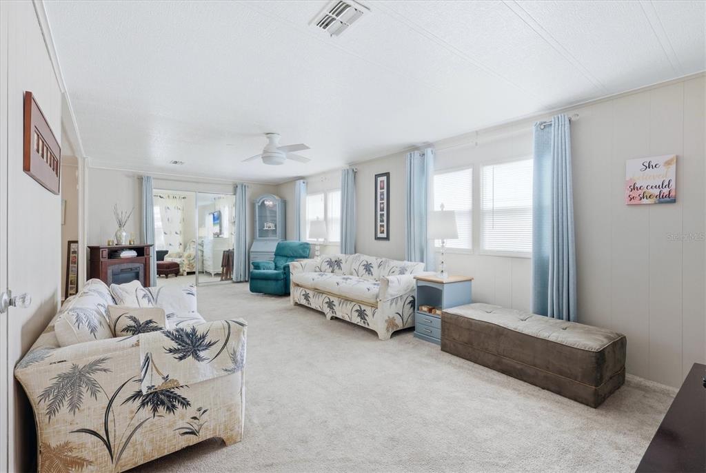 A living room features light-colored walls, carpeted flooring, two palm-print sofas, and blue curtains — 4323 13TH STREET E, ELLENTON, FL