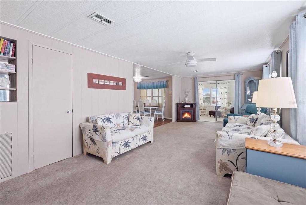 A living room with beige carpet, two patterned sofas, a fireplace, and a dining area beyond — 4323 13TH STREET E, ELLENTON, FL