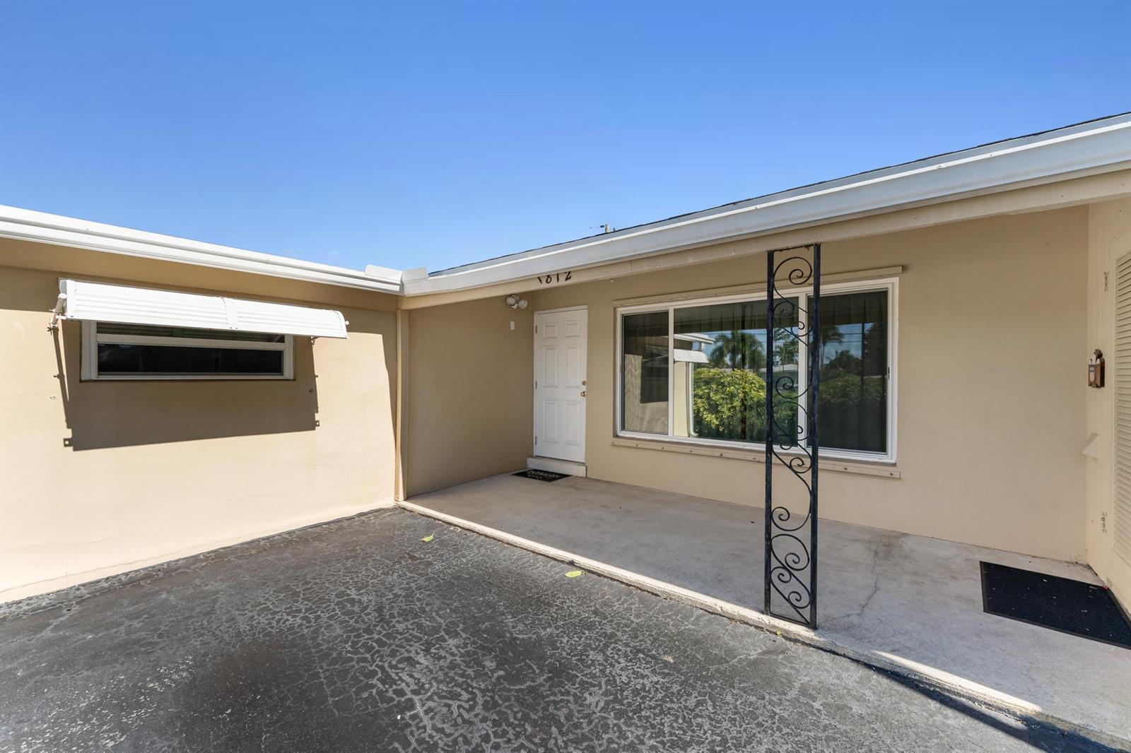 A beige exterior wall features a white front door, a large window, and a metal post — 1812 High Ridge Road, Lake Worth FL 33461, LAKE WORTH, FL