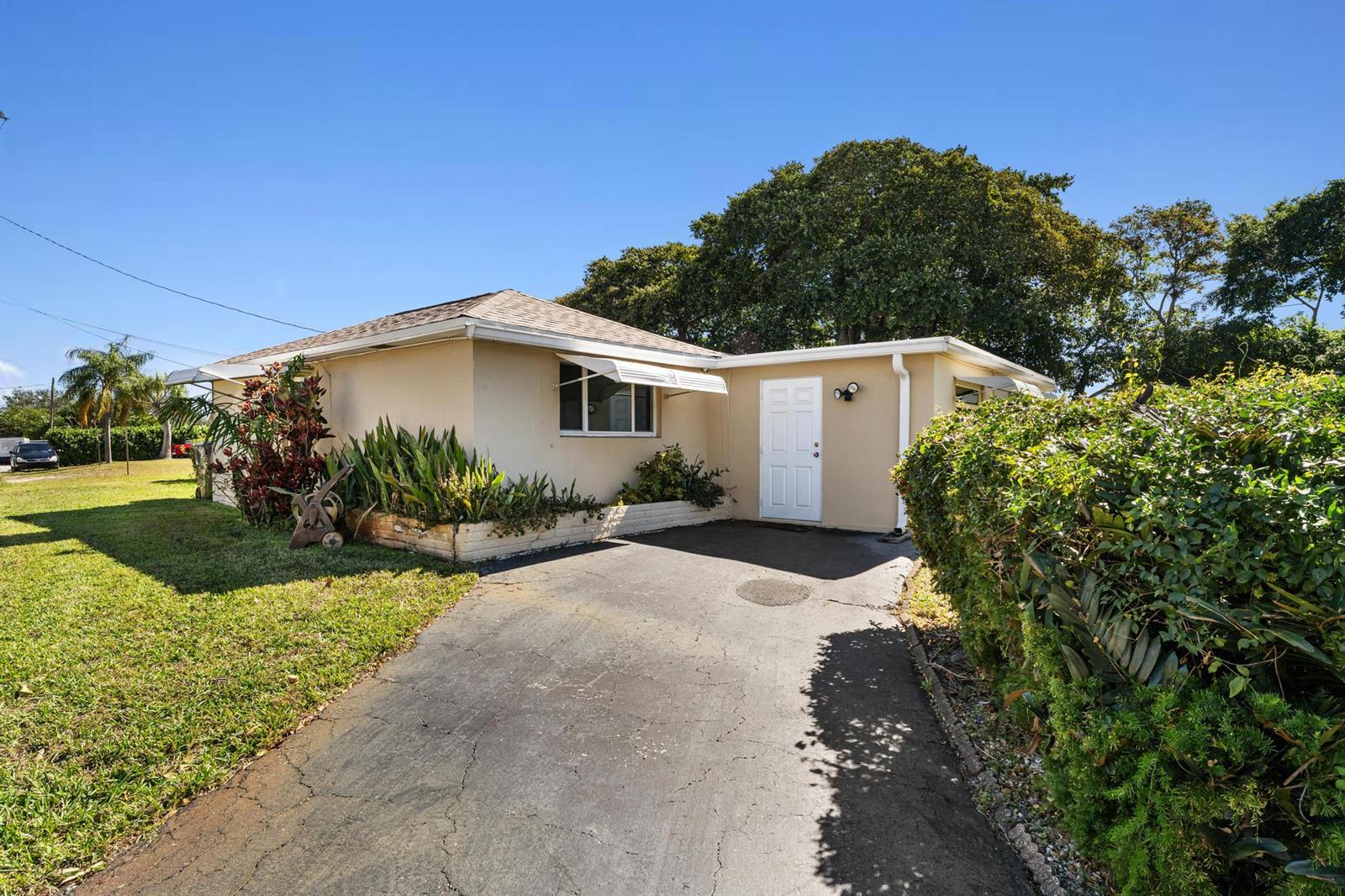 A single-story house with a beige exterior, a white front door, and a paved driveway — 1812 High Ridge Road, Lake Worth FL 33461, LAKE WORTH, FL