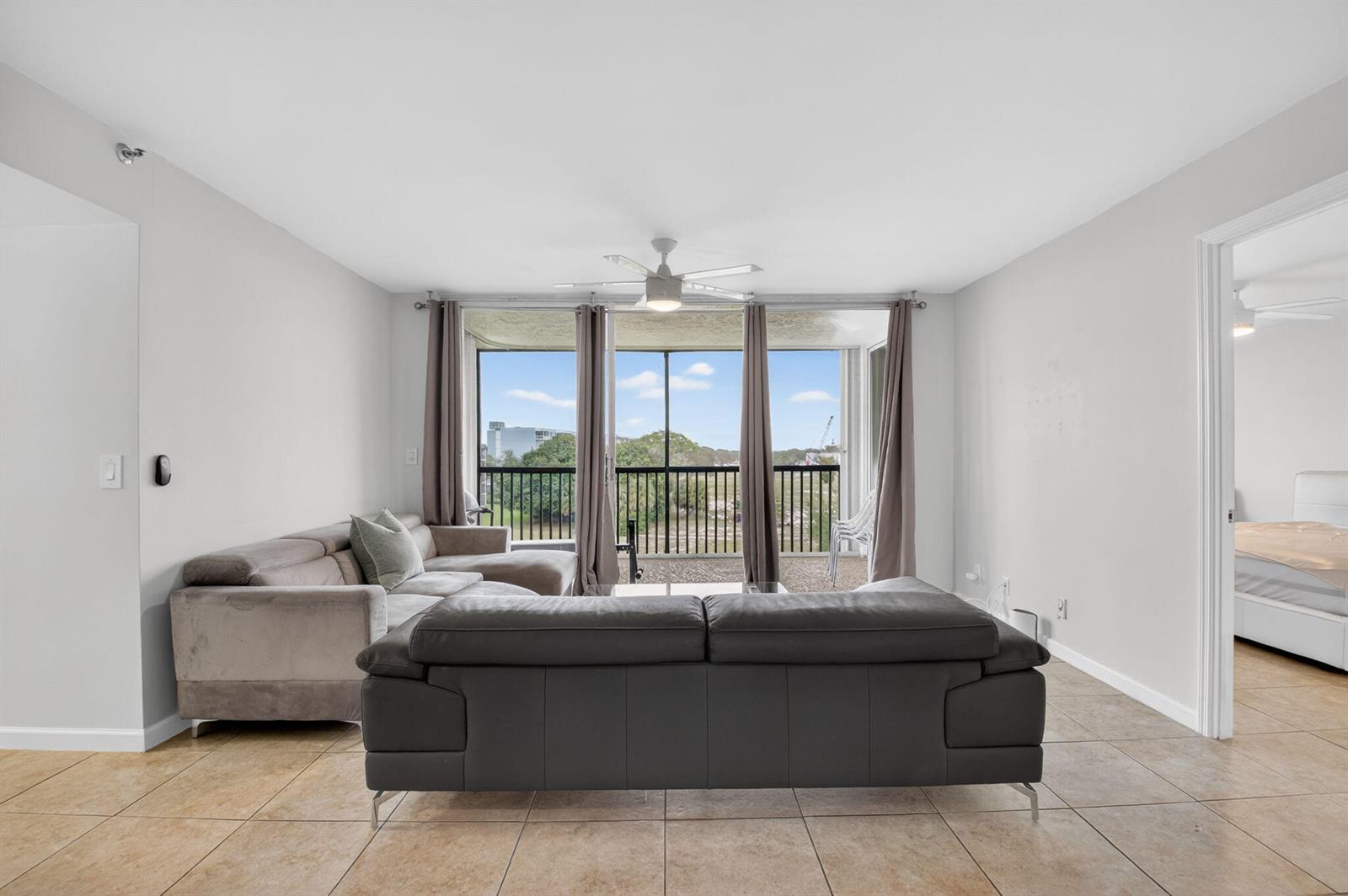 A living room features tile flooring, two sofas, and a balcony with a scenic view — 5280 NW 2nd Ave # 17, Boca Raton FL 33487, BOCA RATON, FL
