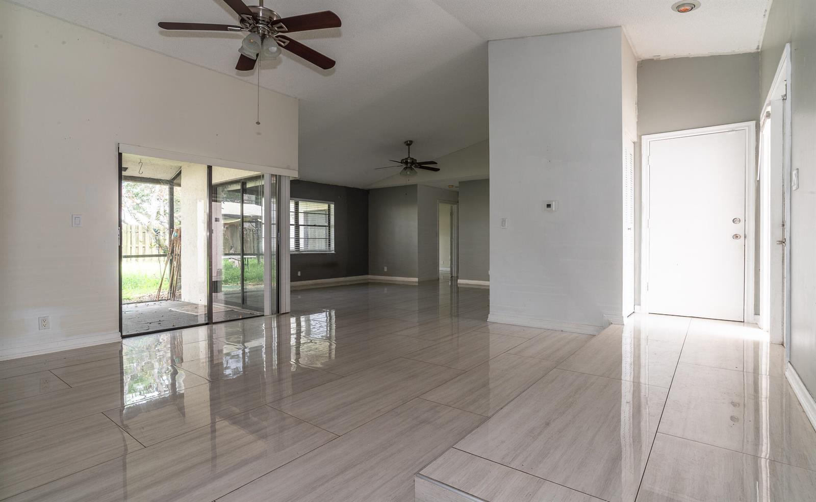 An open-concept living area features light-colored tile flooring, white walls, and sliding glass doors — 11690 Timberwood Road, Boca Raton FL 33428, BOCA RATON, FL