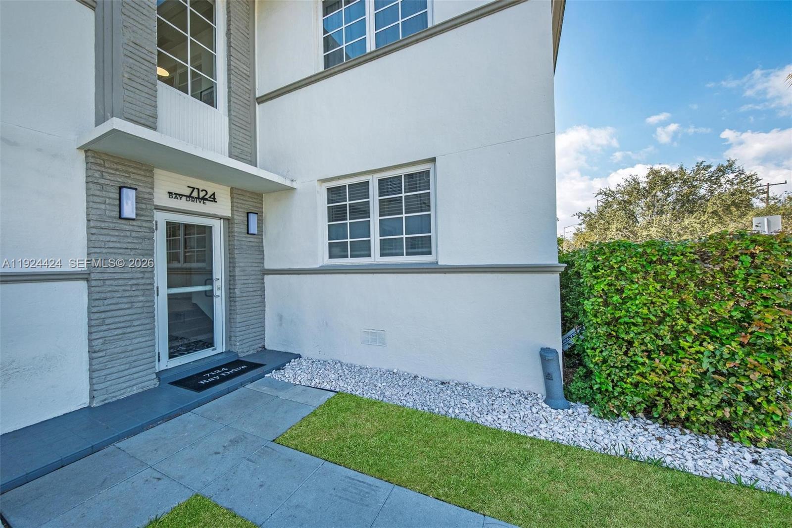 The exterior of a two-story building features a white facade, gray stone accents, and a front entrance — 7124 Bay Dr, Miami Beach FL 33141, MIAMI BEACH, FL