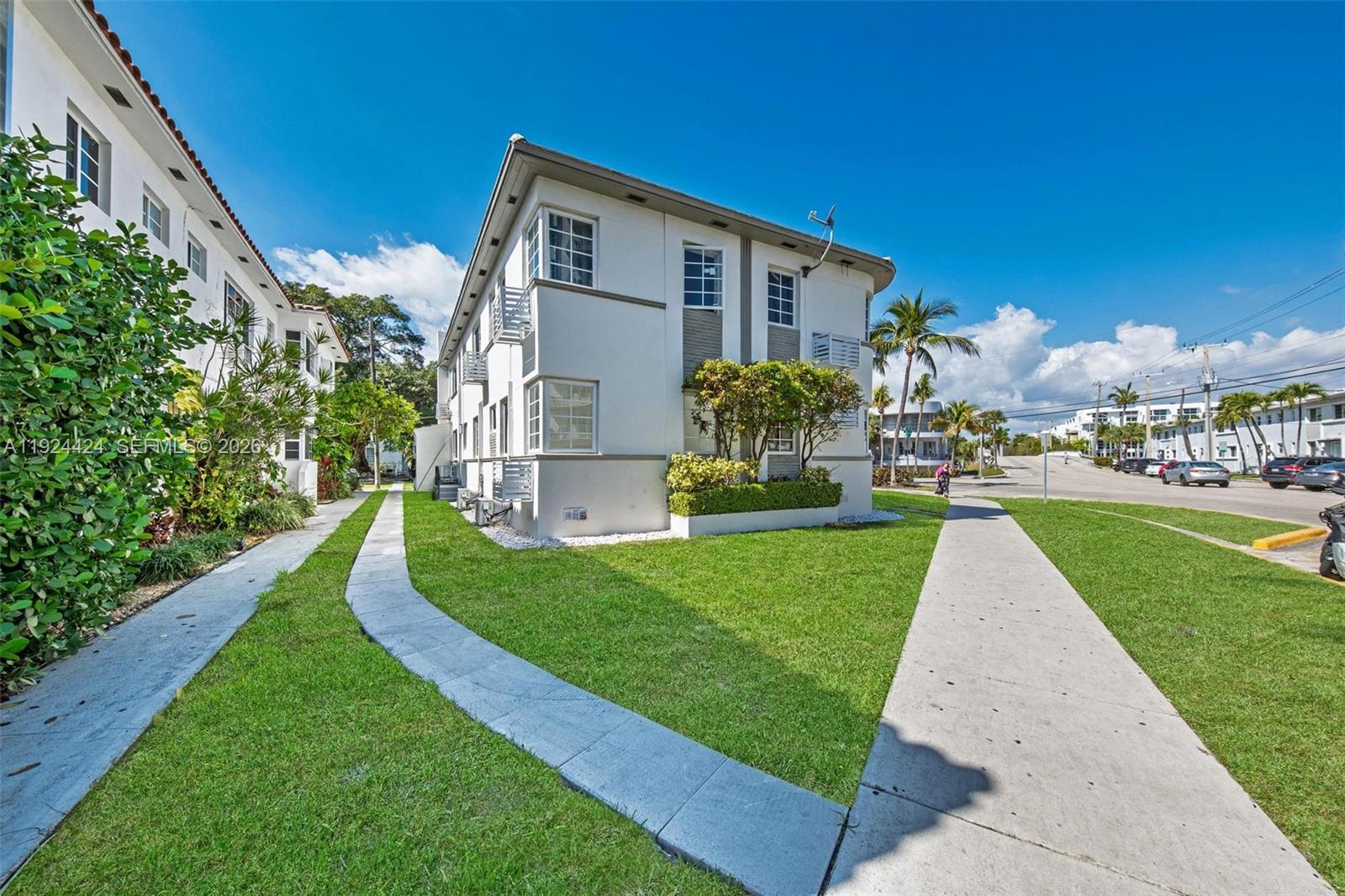 A multi-story apartment building with white stucco walls sits beside a sidewalk and lawn — 7124 Bay Dr, Miami Beach FL 33141, MIAMI BEACH, FL