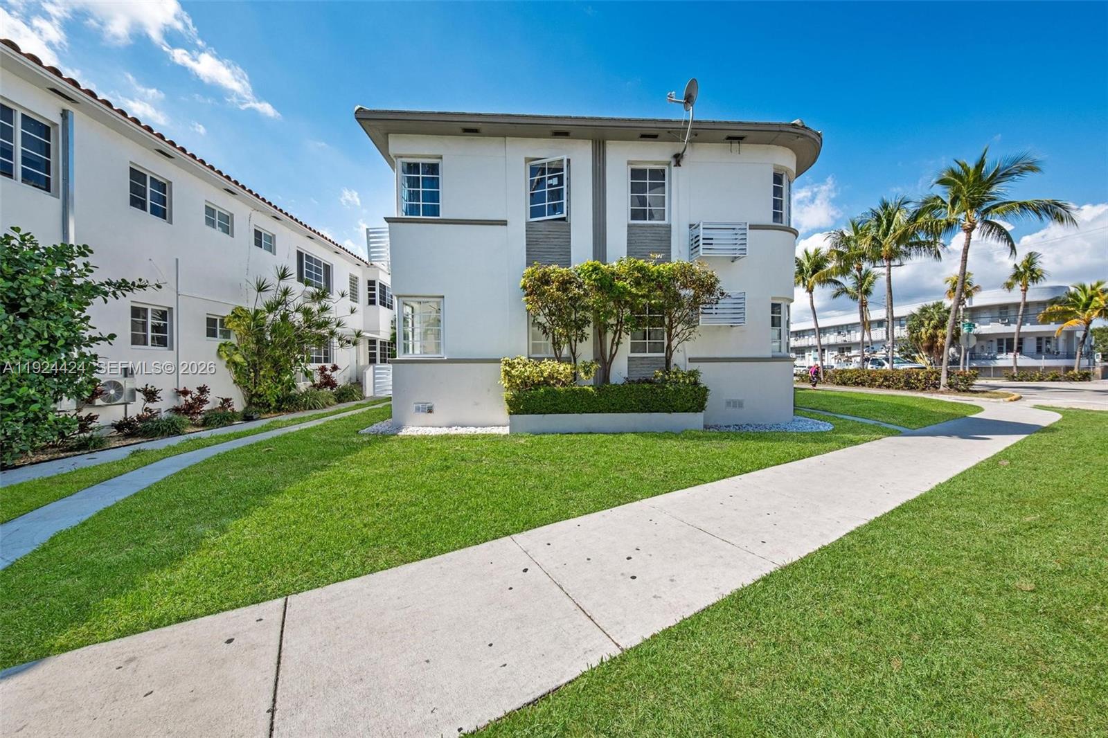 A two-story white apartment building with a curved corner sits on a grassy lawn — 7124 Bay Dr, Miami Beach FL 33141, MIAMI BEACH, FL