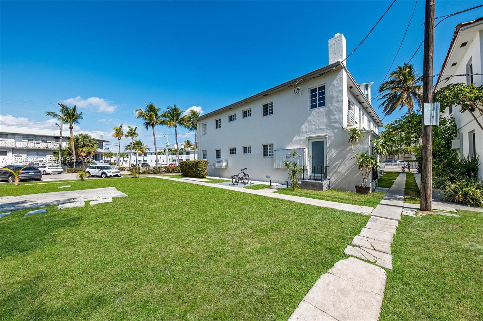 A white two-story apartment building sits next to a grassy lawn and a paved walkway — 7124 Bay Dr, Miami Beach FL 33141, MIAMI BEACH, FL