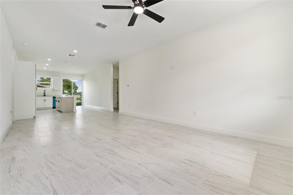 An open-concept living area features white walls, light-colored tile flooring, and a kitchen in the background — 2048 DIXIE AVENUE, SANFORD, FL
