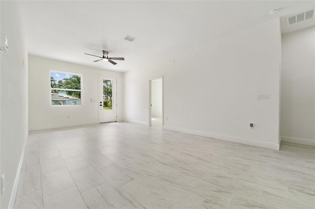 A bright, empty room features white walls, light-colored tile flooring, a ceiling fan, and a door — 2048 DIXIE AVENUE, SANFORD, FL