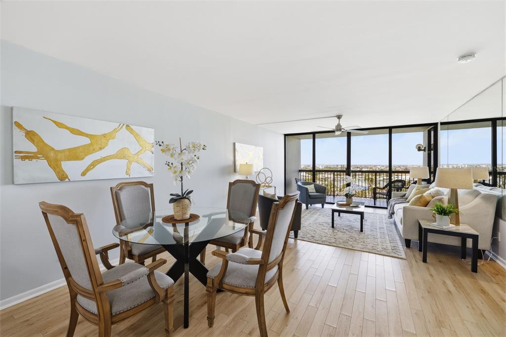 A dining area and living room with a glass table, chairs, and a balcony view — 9495 BLIND PASS ROAD UNIT 905, ST PETE BEACH, FL