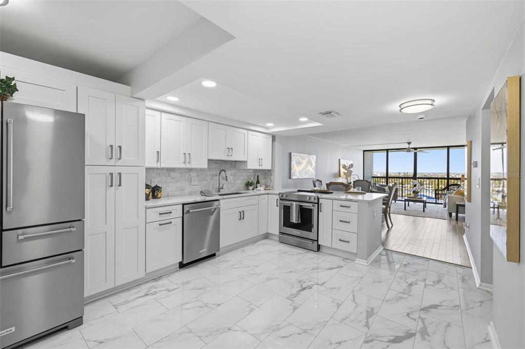A modern white kitchen features stainless steel appliances, marble-look tile flooring, and an open layout — 9495 BLIND PASS ROAD UNIT 905, ST PETE BEACH, FL