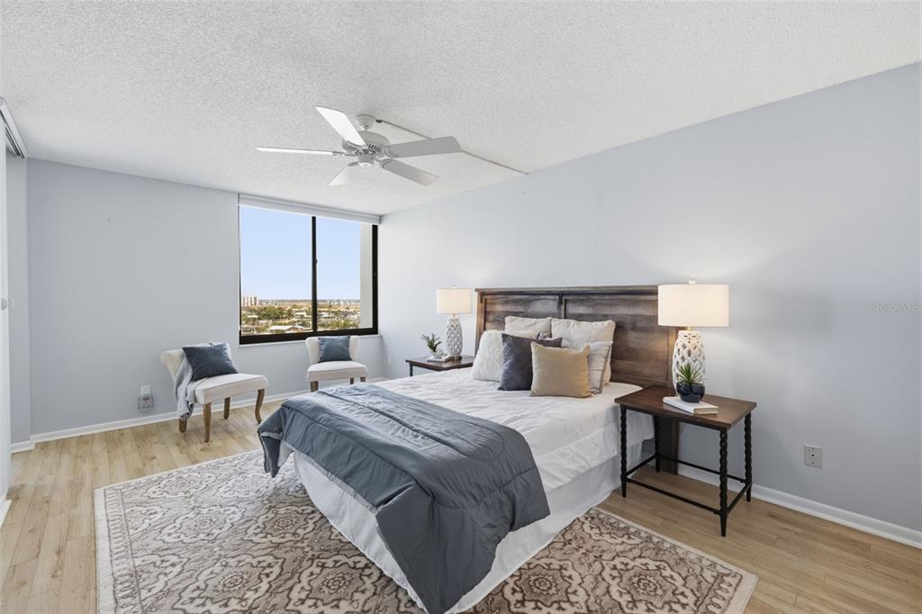 A bedroom features a bed, two nightstands, two chairs, and a large window with views — 9495 BLIND PASS ROAD UNIT 905, ST PETE BEACH, FL
