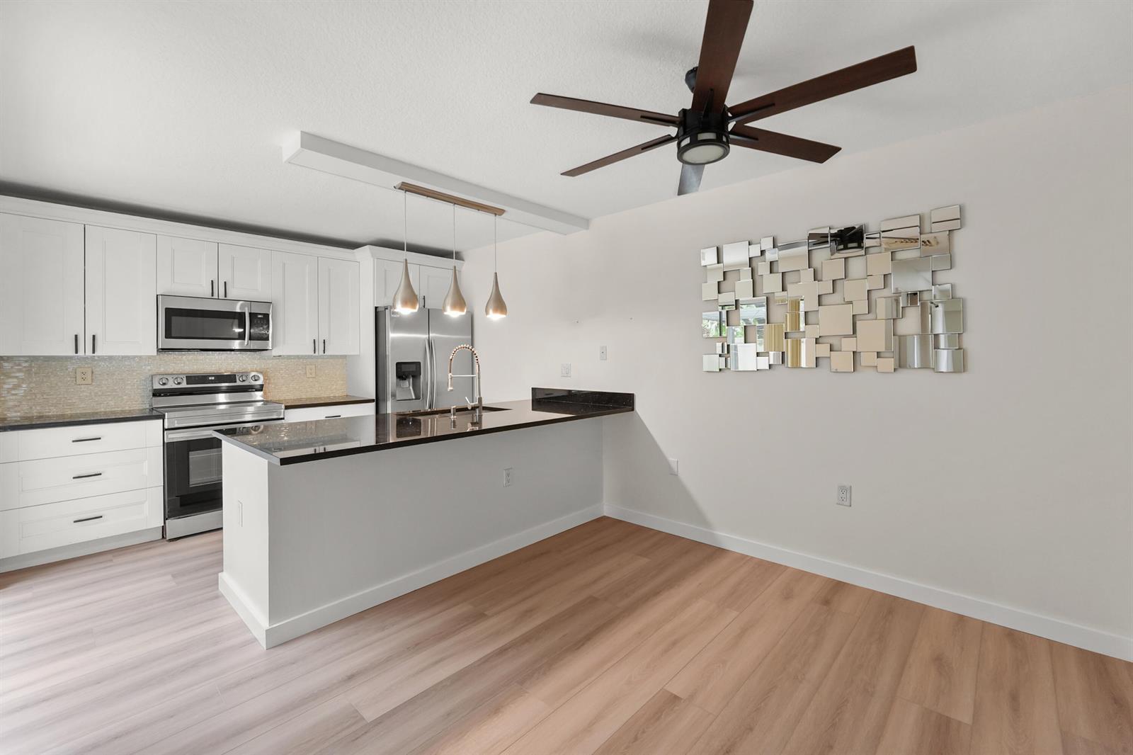 A kitchen features white cabinets, dark countertops, stainless steel appliances, and light wood flooring — 6906 69th Way, West Palm Beach FL 33407, WEST PALM BEACH, FL